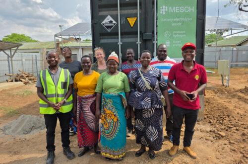 Senior Research Associate Dr Lizzie Ashton with renewable energy engineers and local community members standing in front of the battery-electrolyser test cell, shipped from Loughborough University.