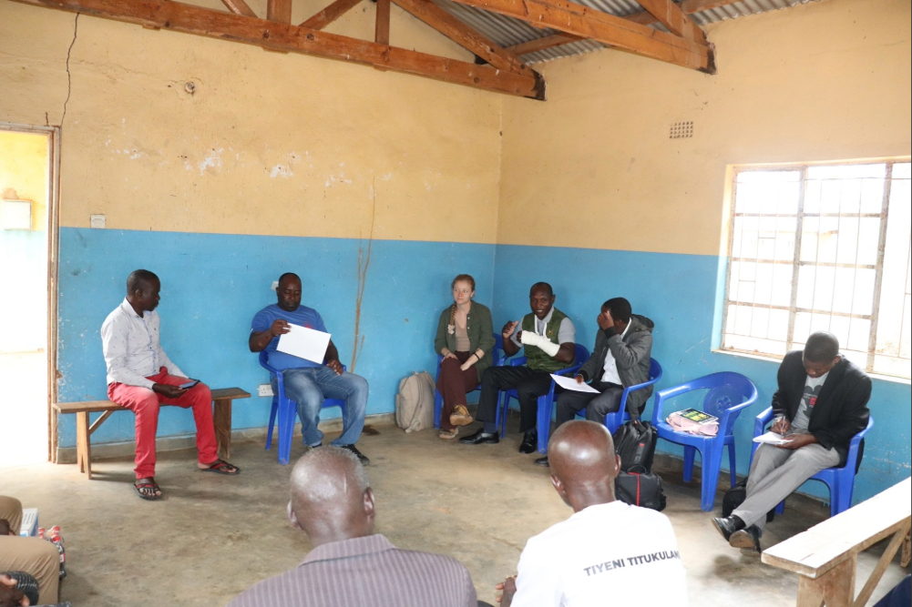 Female engineer with a group of senior chiefs and headmen from a local community in Malawi, sat in a hall